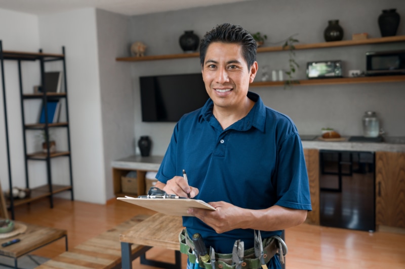 What Is a Plumbing Inspection? Happy plumber working at a house and smiling while writing on a clipboard.