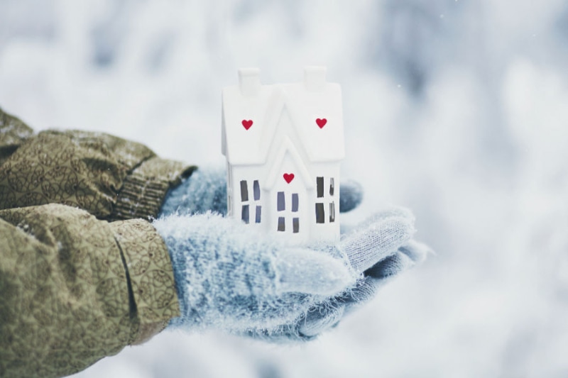 Protect Your Plumbing From Freezing Weather. Image shows two hands wearing mittens and holding a little white wooden house.