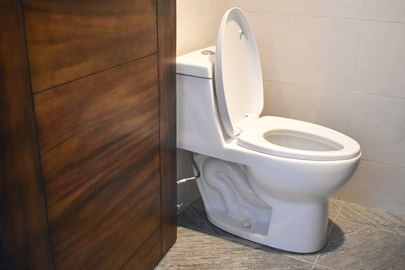 A modern white ceramic toilet is shown in a bathroom setting with its seat down and the lid propped open.
