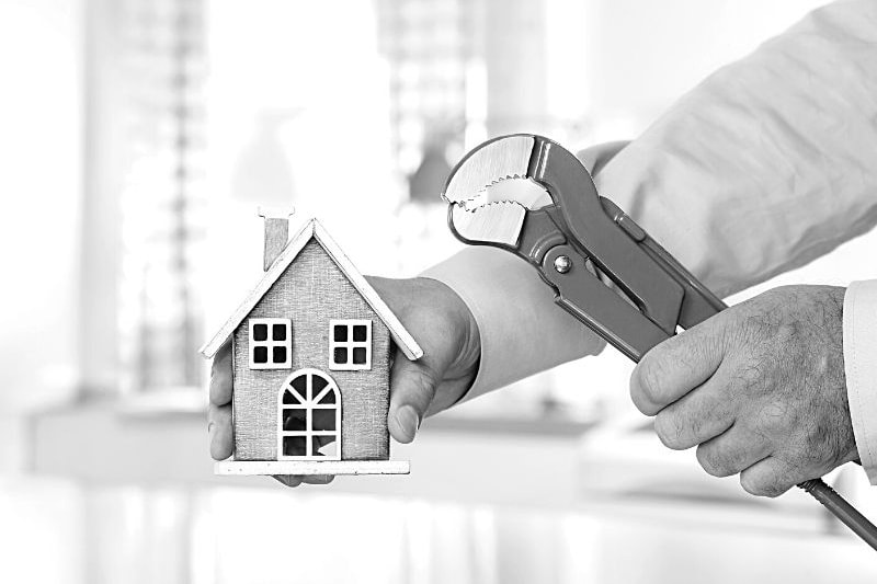 Man holding a model of a house and a wrench.