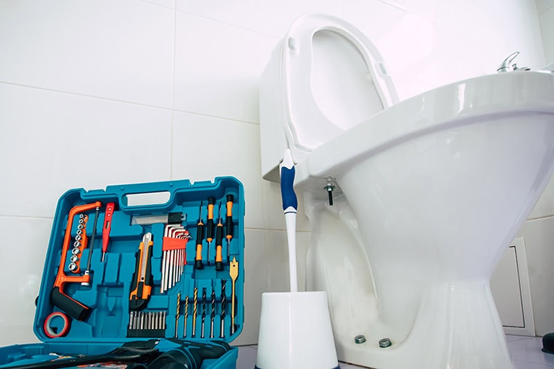 How to Unclog Your Slow-Draining Toilet in University City. Photo of a toilet with tools and a plunger.